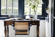 a stylish home office with black window frames, a vintage stained desk, a chic chair and a printed rug, neutral curtains