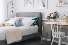 a stylish modern teen bedroom with a grey upholstered bed, pastel and color block bedding, a desk and a chair, some shelves and cool art