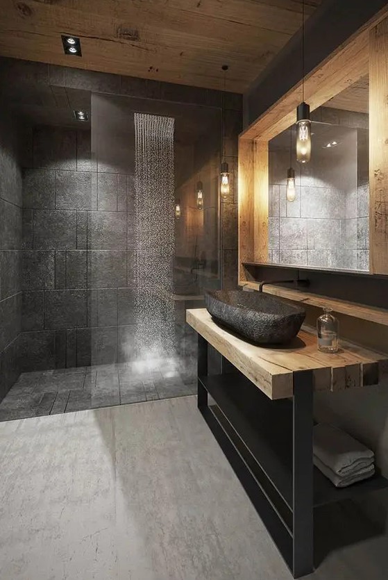 An ultra modern chalet bathroom done with black stone tiles, a bit of blonde wood, blackened metal and a stone sink