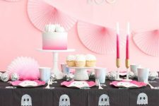 25 a pretty Halloween sweets table in pink and black, with pink paper fans, pink candles and a cake, pink ghost plates and a ghost tablecloth