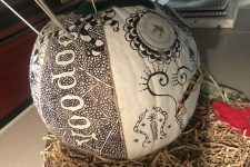31 a white pumpkin decorated with a black sharpie with words, patterns and snakes and with some metal sticks is a unique solution