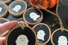 34 black chalkboard tree slice ornaments with white ghosts on them are a cute rustic Halloween decor idea