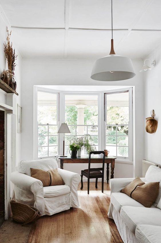 A bay window with a dark stained desk and a chair for working here, neutral vintage furniture and a pendant lamp