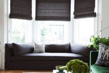 a bay window with a fitted sofa and pillows, dark shades makes this space cozy to be and welcomes a lot