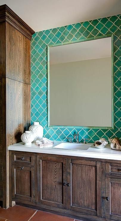 A bold bathroom with green arabesque tiles, dark stained furniture, a large mirror and white stone countertops