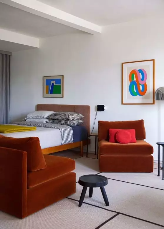 a bold bedroom with a wooden bed, terracotta chairs, bright art and color blocking catches an eye with each item