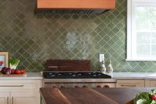 a bold kitchen with neutral shaker style cabinetry, a green arabesque tile backsplash, an orange hood and a green kitchen island with butcheblock countertops