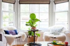 a bright boho sitting zone by the bay window – metal chais with pillows and faux fur, a potted plant and a window with Roman shades