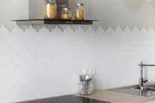a contemporary white kitchen with neutral butcherblock countertops, sleek modern appliances, an arabesque tile backsplash and pendant lamps