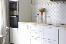 a contemporary white kitchen with shaker cabinets, butcherblock countertops, a white arabesque tile backsplash, pendant bulbs is chic
