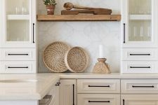 a creamy-colored kitchen with shaker style cabinets, lit up shelves and a large scale arabesque tile backsplash