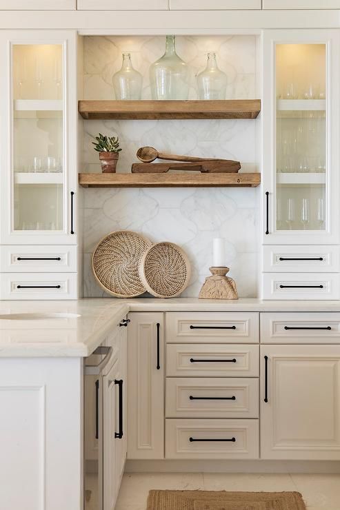 A creamy colored kitchen with shaker style cabinets, lit up shelves and a large scale arabesque tile backsplash