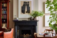 a lovely home office with neutral walls, a black fireplace, a dark stained desk and a chair, a rich-stained bookcase and a chair plus greenery