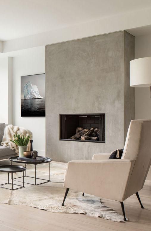 a neutral living room with a concrete fireplace, neutral seating furniture, black coffee tables and potted blooms