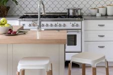 a pretty and catchy white kitchen with a white arabesque tile backsplash, grey stone countertops, stainless steel appliances and an ornated hood