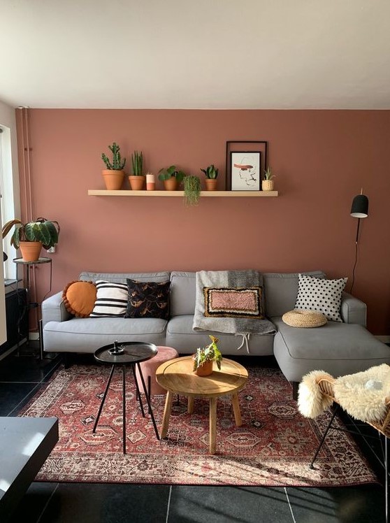 a pretty boho living room with a terracotta statement wall, a grey sectional, a rattan chair and some potted plants and round tables