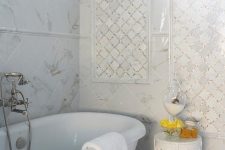a refined white bathroom clad with white marble tiles and white arabesque tiles accented with shiny gold grout