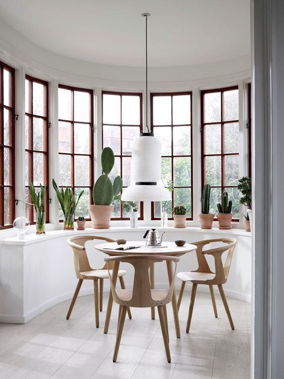 a round bay window with a large console table for displaying plants, a breakfast zone with a round table and some chairs