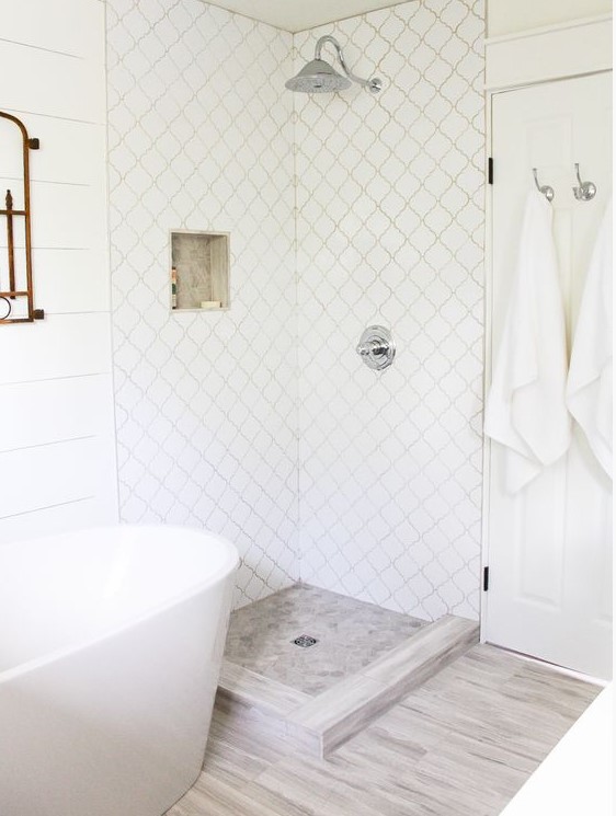 a serene neutral bathroom with wood inspired tiles on the floor, white arabesque tiles in the shower and white planked walls looks very chic