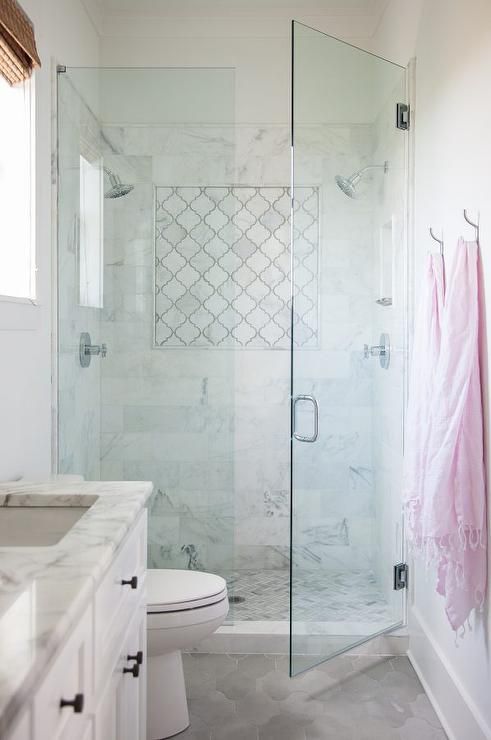 a small and chic neutral bathroom with white marble and arabesque tiles, a small shower enclosed in glass, a white vanity and stainless steel fixtures