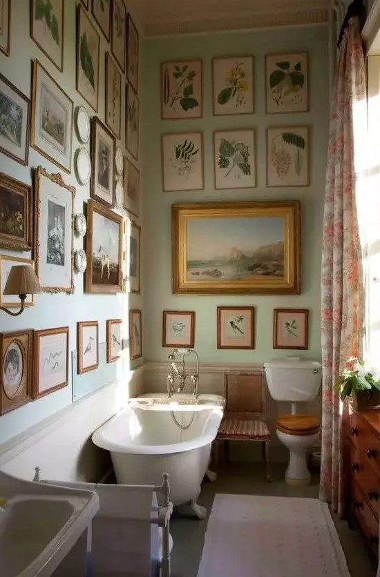 A vintage bathroom with light green walls, a gallery wall that covers two walls at once, a clawfoot bathtub and a free standing sink