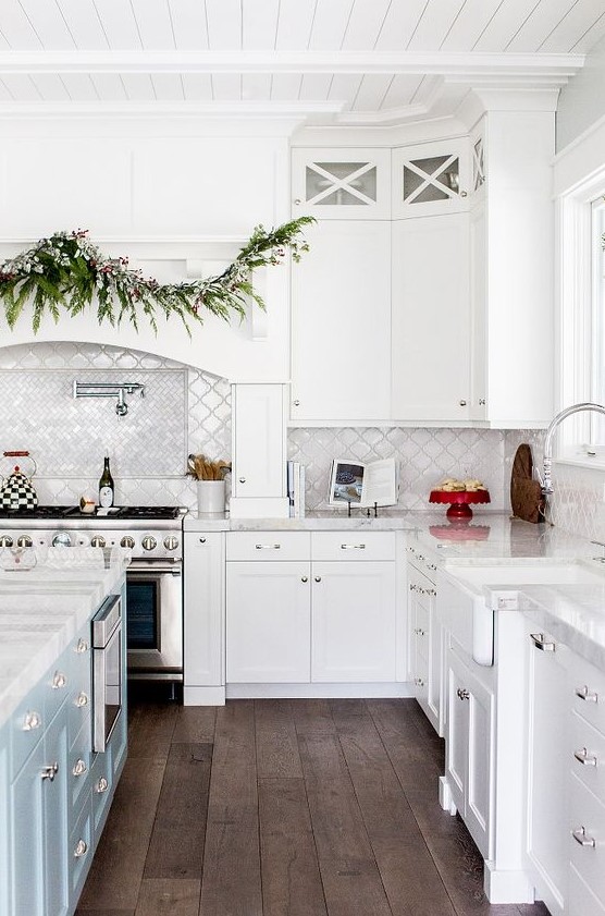 a white farmhouse kitchen with a pale blue kitchen island, a white arabesque tile backsplash and chevron tiles over the cooker is a lovely idea
