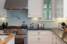 a white kitchen with black countertops, a light blue arabesque tile backsplash, stainless steel appliances and knobs