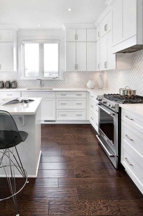 a white modern kitchen with shaker cabinets, a white small scale arabesque tile backsplash, black sheer stools and shiny fixtures