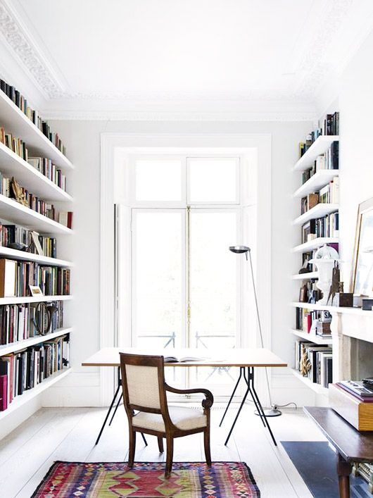an airy white home office with built-in bookshelves, a delicate desk, a vintage chair and a bold printed rug