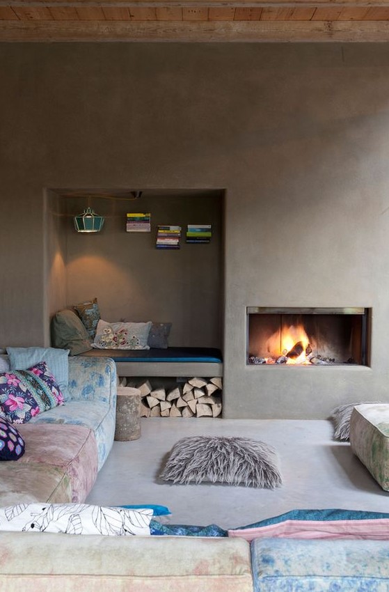 An unusual living room with concrete walls and a built in fireplace, a niche for storage and a daybed, colorful furniture