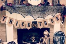 a chic Halloween fireplace with black spiderwebs, branches, bats, candles, a skeleton, a plaque skull and a banner