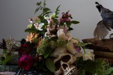 05 a moody Halloween centerpiece of a skull plus some blush and purple blooms and greenery and herbs