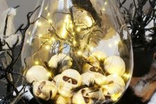 11 a Halloween terrarium of a large jar, skulls and lights, branches and spiderweb, a blackbird is a stylish idea for moody decor