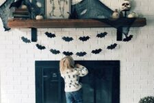 13 a Halloween mantel decorated with black paper bat buntings, black spider web and pumpkins plus skulls