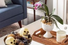 19 a chic Halloween coffee table with a potted bloom, a bowl with spiders, skulls and pinecones and some bones in a shell
