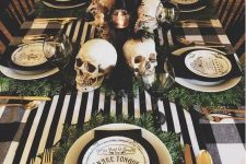 23 a Halloween tablescape with black and white linens, gold cutlery, skulls, candles and printed plates plus greenery