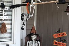30 a Halloween porch with skeletons sitting on the lounger and broom, with witches’ hats, signs and lanterns