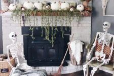 35 a neutral Halloween fireplace decorated with greenery and white pumpkins, with a skeleton scene in front of it is a cool idea