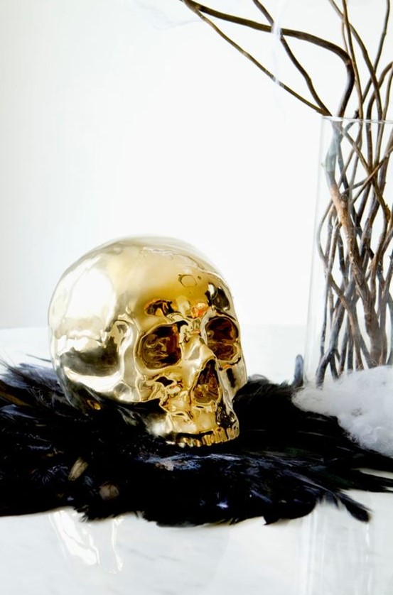 bold Halloween decor with black feathers, a gilded skull, branches in a vase is a chic and beautiful idea for glam Halloween