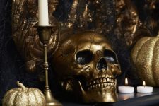 39 glam black and gold Halloween decor with gold glitter pumpkins, a gold skull, gold candlesticks and white candles, faux black blooms