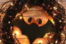 41 a black vine Halloween wreath with lights, orange blooms, a large black paper bat is a cool solution to DIY easily