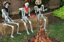 45 an outdoor Halloween scene with skeletons sitting around the fire made of branches and lights is a cool idea for your outdoor space
