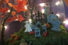a graveyard pumpkin diorama with moss, mini pumpkins, tombstones, a ghost, lights and a fall tree is a great idea for Halloween
