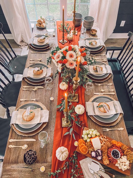a beautiful bright Thanksgiving tablescape with an orange table runner and candles, white pumpkins and orange and white flowers