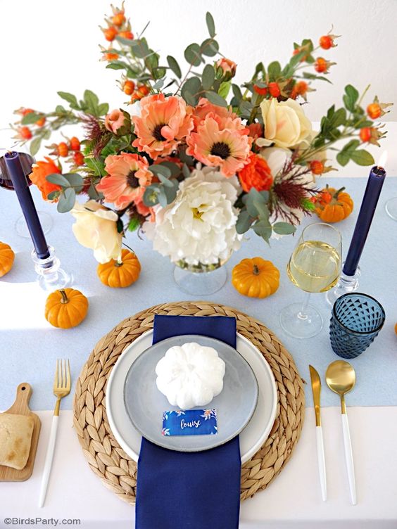 a bold and contrasting orange and navy Thanksgiving place setting with a navy napkin and candles, orange pumpkins and blooms