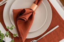 37 a stylish and laconic Thanksgiving place setting with a rust placemat and a napkin, white plates and a copper napkin ring