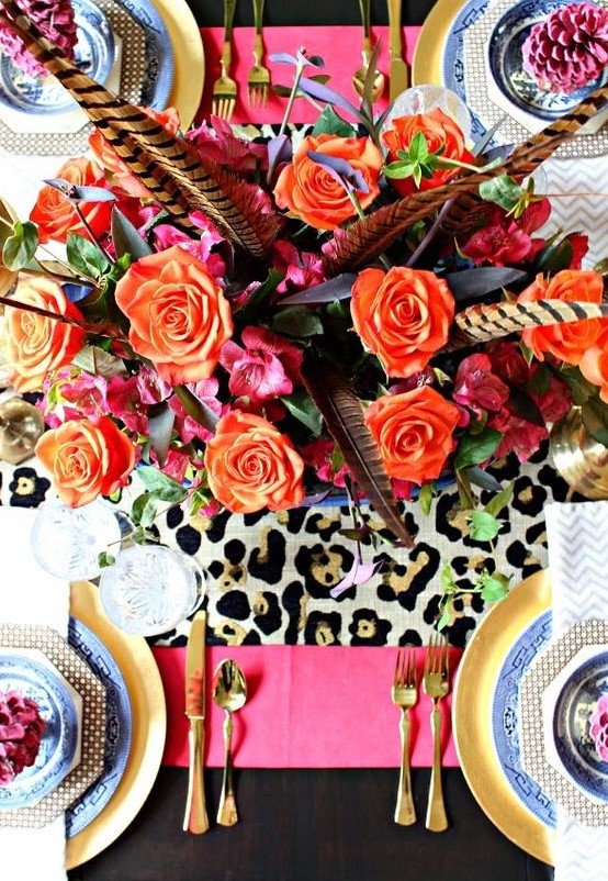 a super bold Thanksgiving tablescape with blue and gold plates, a leopard and hot pink table runner, orange blooms and feathers
