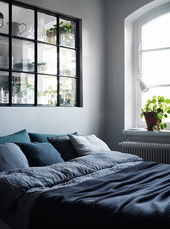 A Scandinavian bedroom connected to the kitchen with a large window with a black frame looks peaceful and light filled
