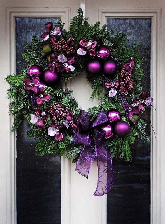 a beautiful and lush Christmas wreath decorated with purple ornaments, purple faux berries and blooms and a large purple ribbon bow