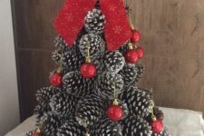 a cone-shaped Christmas tree made of snowy pinecones, decorated with red ornaments and topped with a red bow
